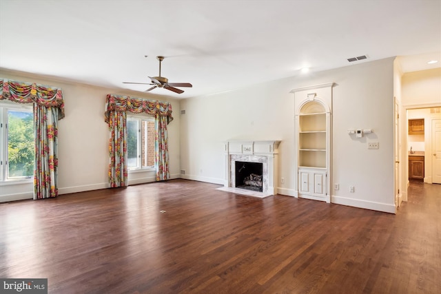 unfurnished living room with a high end fireplace, dark wood-type flooring, and ceiling fan