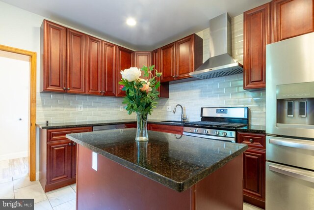 kitchen with stainless steel appliances, sink, wall chimney exhaust hood, dark stone counters, and a kitchen island