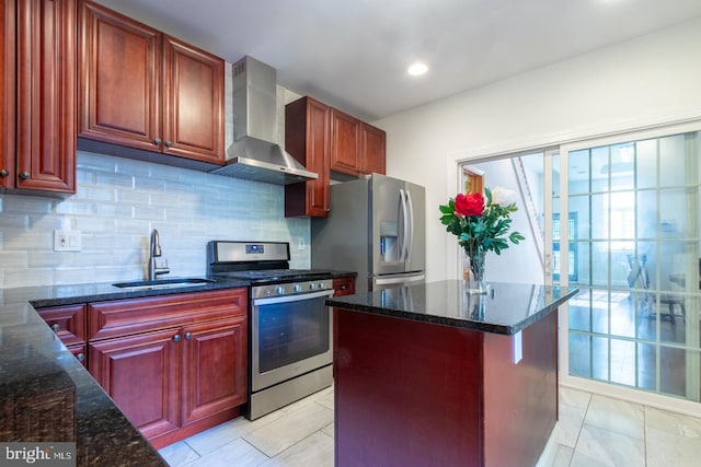 kitchen with a center island, stainless steel appliances, sink, dark stone countertops, and wall chimney range hood