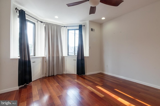 unfurnished room with a healthy amount of sunlight, ceiling fan, and dark wood-type flooring