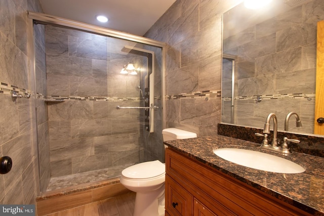 bathroom featuring toilet, vanity, wood-type flooring, tile walls, and a shower with shower door