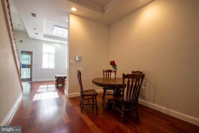 dining space with crown molding, dark wood-type flooring, and a raised ceiling