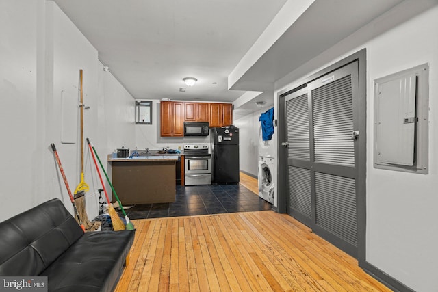 kitchen featuring electric panel, black appliances, stacked washer / drying machine, sink, and dark hardwood / wood-style floors