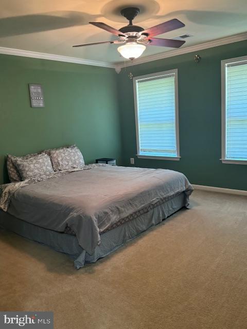 carpeted bedroom featuring baseboards, visible vents, ornamental molding, and a ceiling fan