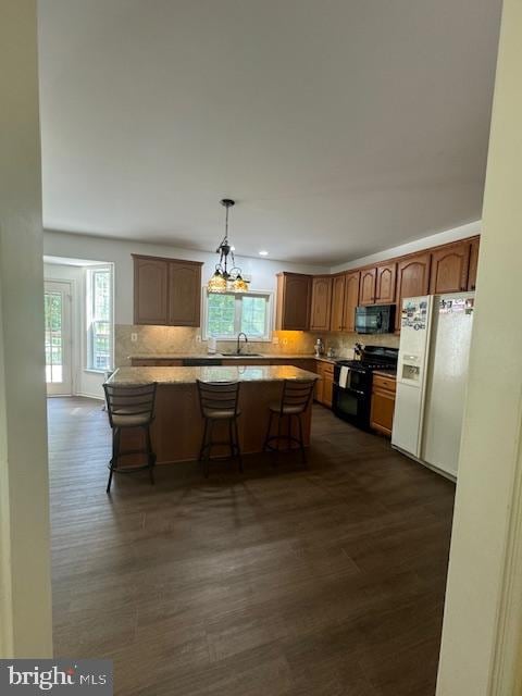 kitchen featuring a kitchen bar, black appliances, sink, hanging light fixtures, and dark wood-type flooring