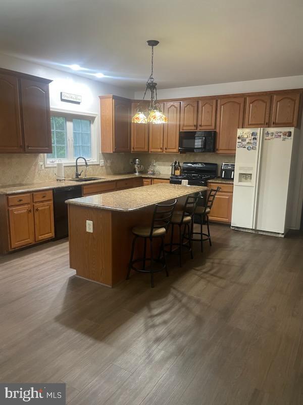 kitchen featuring dark hardwood / wood-style floors, black appliances, a kitchen island, and pendant lighting