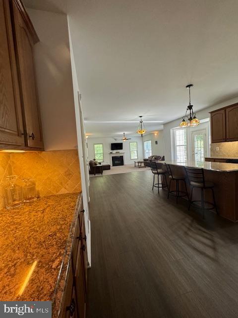 kitchen featuring a breakfast bar, dark wood-style flooring, a fireplace, decorative backsplash, and open floor plan