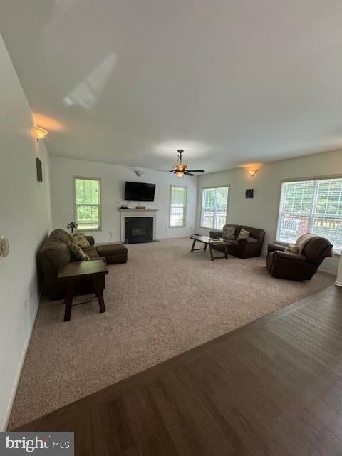 living room with a fireplace, carpet flooring, ceiling fan, wood finished floors, and baseboards