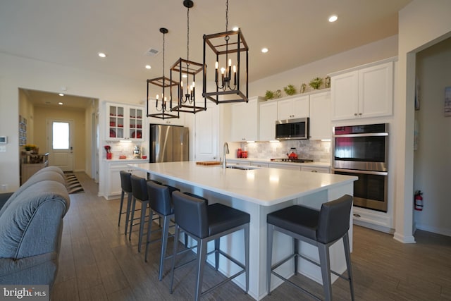 kitchen featuring decorative light fixtures, appliances with stainless steel finishes, white cabinetry, dark hardwood / wood-style floors, and a kitchen island with sink