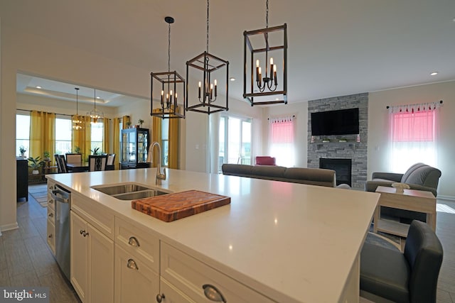 kitchen with white cabinets, sink, a stone fireplace, dark wood-type flooring, and a kitchen island with sink