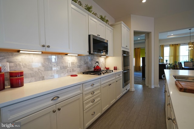 kitchen with backsplash, stainless steel appliances, decorative light fixtures, dark hardwood / wood-style flooring, and white cabinets