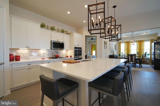 kitchen featuring dark wood-type flooring, white cabinets, stainless steel appliances, and a center island with sink