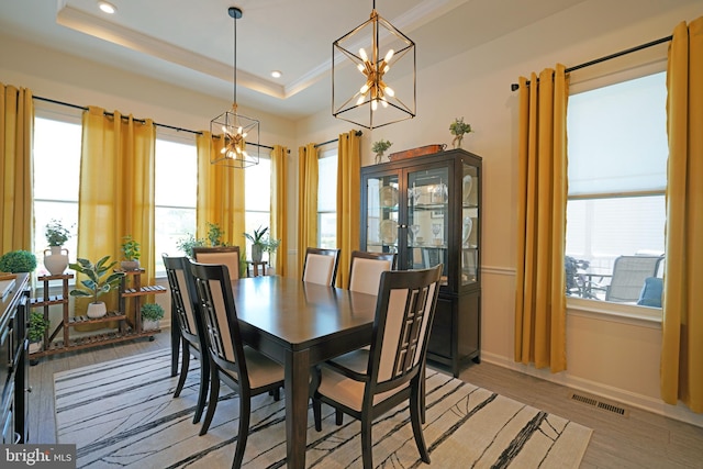 dining space with light hardwood / wood-style floors, a tray ceiling, a wealth of natural light, and a chandelier