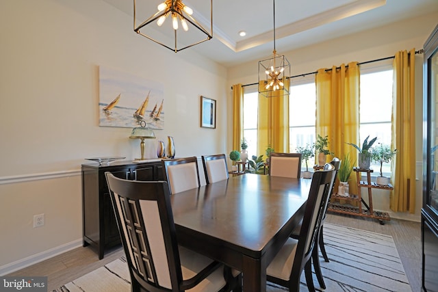 dining space featuring a raised ceiling, light hardwood / wood-style floors, a notable chandelier, and a healthy amount of sunlight