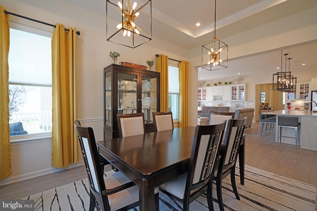 dining room featuring crown molding, an inviting chandelier, light hardwood / wood-style floors, and a raised ceiling