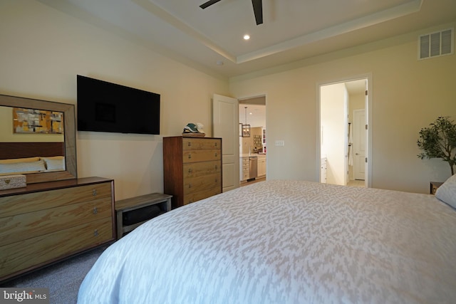 bedroom with carpet, ceiling fan, a raised ceiling, and connected bathroom