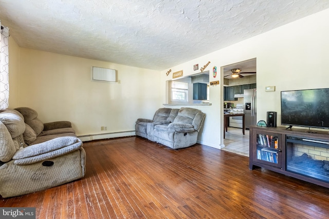 living room featuring ceiling fan, baseboard heating, hardwood / wood-style floors, and a textured ceiling