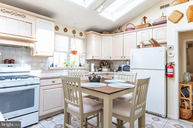 kitchen featuring visible vents, light countertops, vaulted ceiling with skylight, light tile patterned flooring, and white appliances