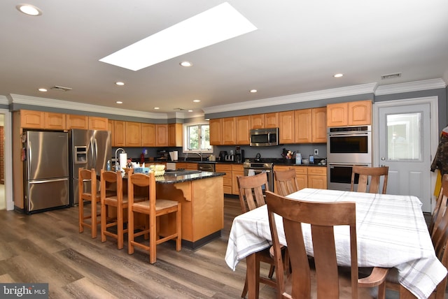 kitchen with ornamental molding, a skylight, stainless steel appliances, dark hardwood / wood-style floors, and a center island with sink