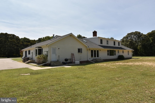 back of house with cooling unit, a lawn, entry steps, and a chimney