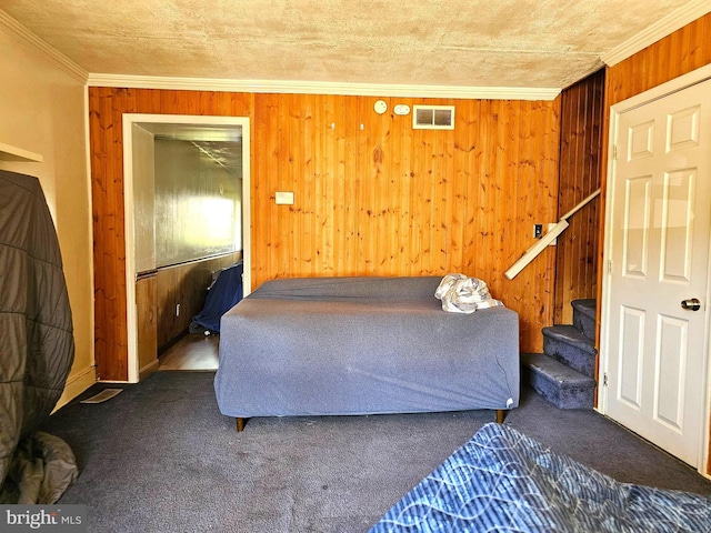 carpeted bedroom with visible vents, wooden walls, crown molding, and a textured ceiling