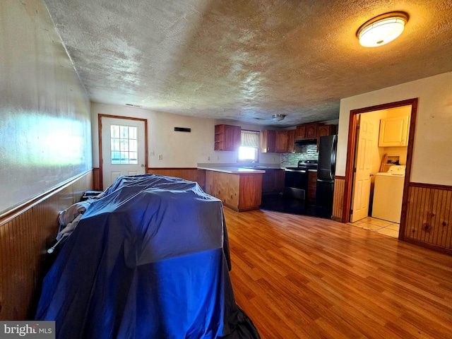 interior space with a wealth of natural light, stainless steel electric stove, washer / clothes dryer, and a wainscoted wall