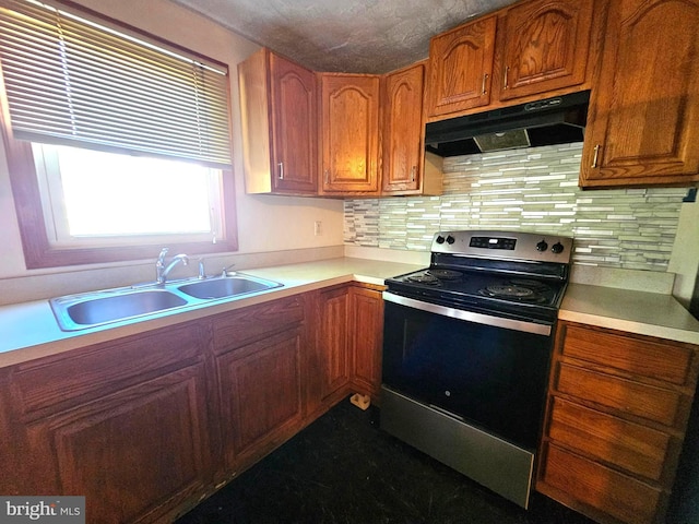 kitchen with a sink, stainless steel range with electric cooktop, light countertops, under cabinet range hood, and backsplash