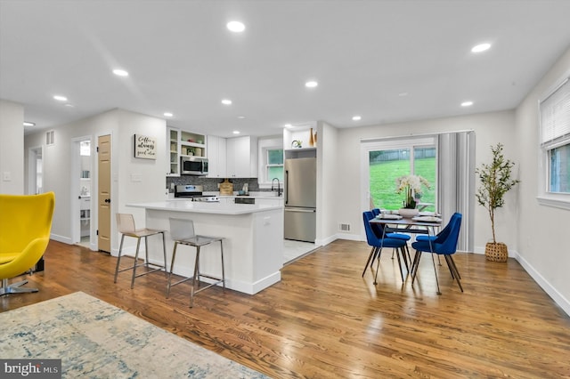 kitchen with light wood-type flooring, a breakfast bar, backsplash, appliances with stainless steel finishes, and white cabinetry