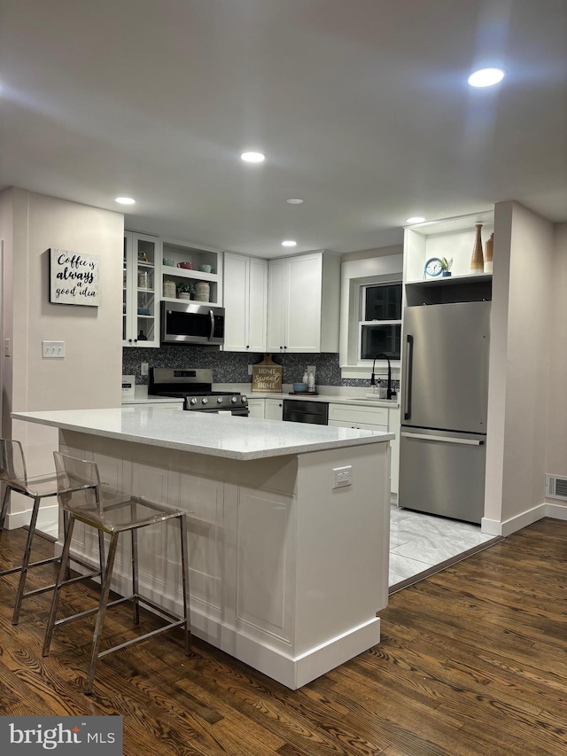 kitchen featuring light stone countertops, white cabinets, dark wood-type flooring, appliances with stainless steel finishes, and a kitchen breakfast bar