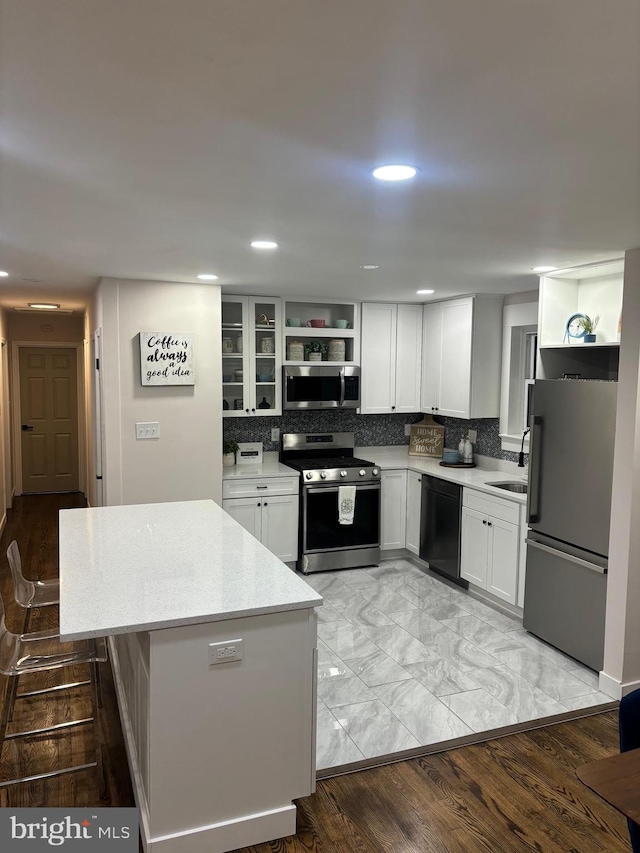 kitchen featuring light stone counters, white cabinets, stainless steel appliances, light hardwood / wood-style floors, and decorative backsplash