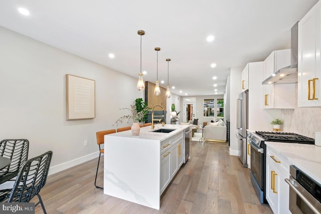 kitchen featuring white cabinetry, premium appliances, decorative light fixtures, a kitchen island with sink, and sink