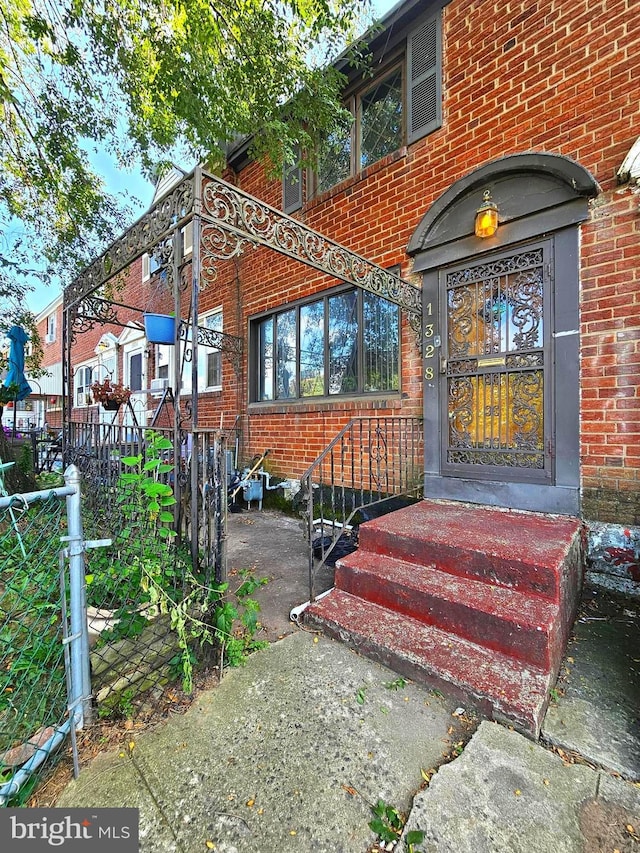 view of exterior entry with brick siding and fence