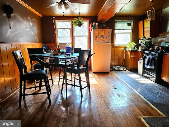 dining room with ceiling fan, wood-type flooring, and wooden walls