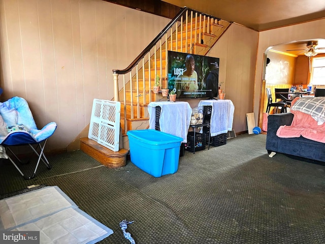 carpeted living room with ceiling fan and wooden walls