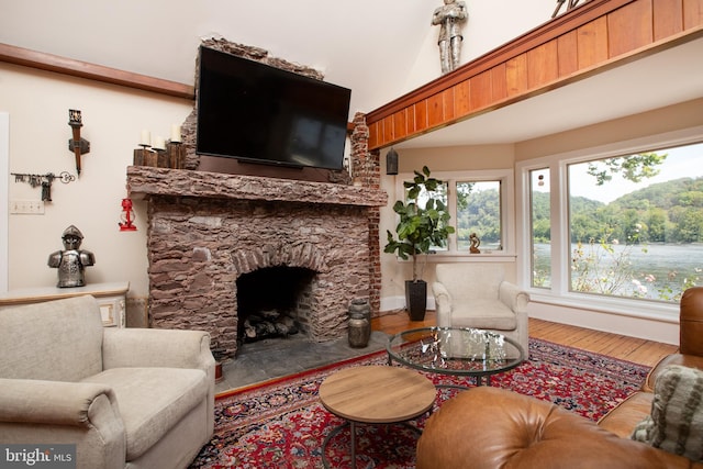 living room featuring lofted ceiling, wood-type flooring, and a stone fireplace