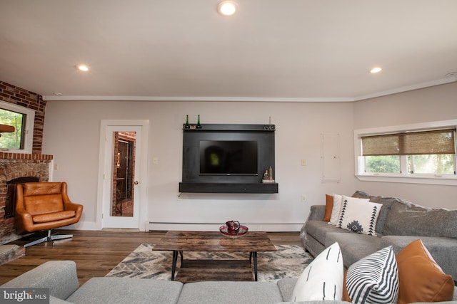 living room featuring a baseboard heating unit, hardwood / wood-style flooring, ornamental molding, and a brick fireplace