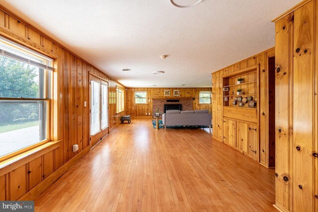 interior space with a fireplace, light wood-type flooring, a textured ceiling, and wood walls