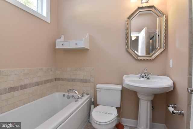 bathroom with toilet, a garden tub, and baseboards