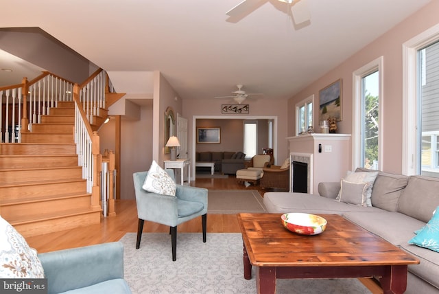 living area featuring a ceiling fan, wood finished floors, a fireplace, and stairs