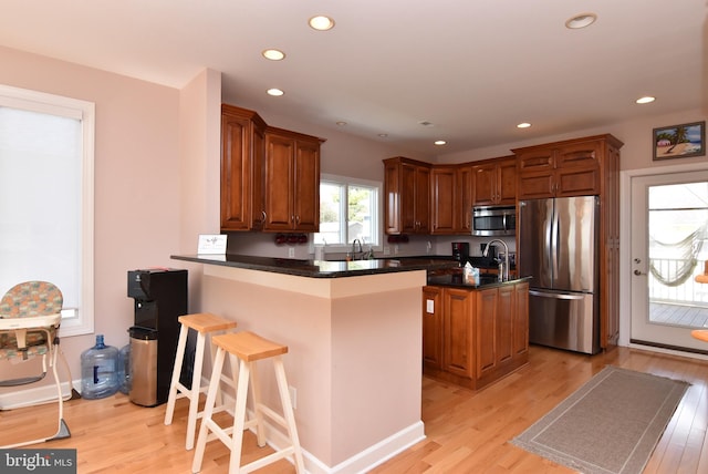 kitchen featuring appliances with stainless steel finishes, light hardwood / wood-style floors, kitchen peninsula, a kitchen bar, and a center island