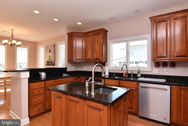 kitchen with a peninsula, a sink, stainless steel dishwasher, dark stone counters, and an island with sink