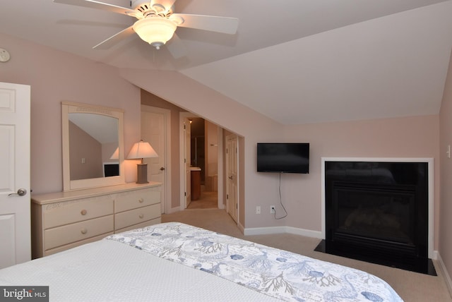 bedroom with baseboards, light colored carpet, lofted ceiling, a fireplace with flush hearth, and ceiling fan