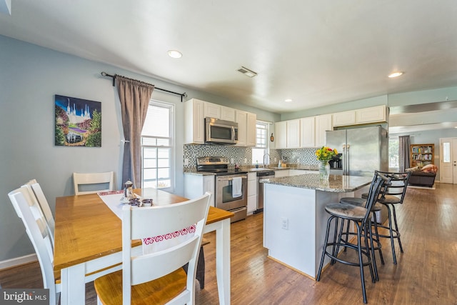 kitchen featuring a kitchen island, appliances with stainless steel finishes, decorative backsplash, hardwood / wood-style flooring, and dark stone countertops