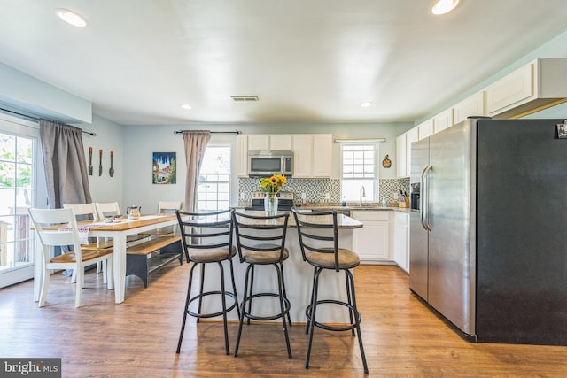 kitchen with wood-type flooring, tasteful backsplash, stainless steel appliances, sink, and white cabinets