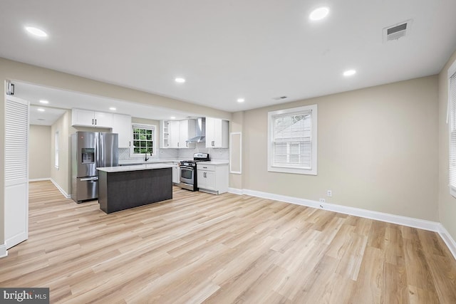 kitchen with white cabinets, appliances with stainless steel finishes, a kitchen island, and wall chimney range hood