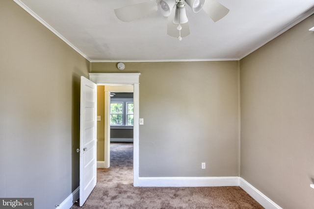 carpeted spare room with a ceiling fan, baseboards, and crown molding