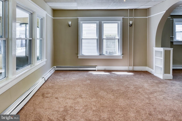 unfurnished room featuring a wealth of natural light, carpet flooring, arched walkways, and a baseboard radiator