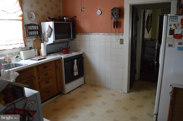 kitchen featuring wallpapered walls, electric range, brown cabinetry, freestanding refrigerator, and tile walls