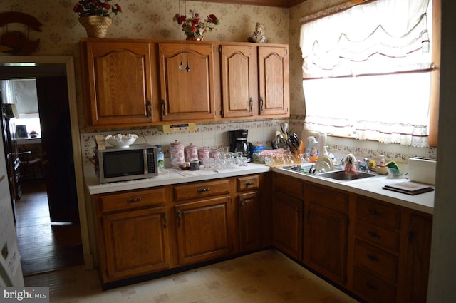 kitchen featuring wallpapered walls, stainless steel microwave, brown cabinets, light countertops, and a sink