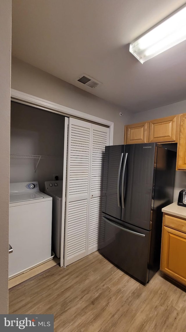 kitchen with light wood-type flooring, washer and clothes dryer, and black fridge